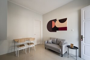 Una sala moderna con un sofá gris, una mesa de comedor de madera con sillas y una obra de arte abstracta de gran formato en la pared.