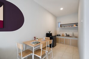 A compact kitchen with a dining area, featuring a refrigerator, a sink, and a small shelf with kitchenware.