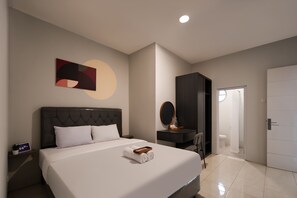 A modern hotel room with a large bed, a desk with a mirror, and a door leading to a bathroom.