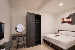 A modern hotel room with a bed, a desk with a chair, a wardrobe, a mirror, and a wall art piece.