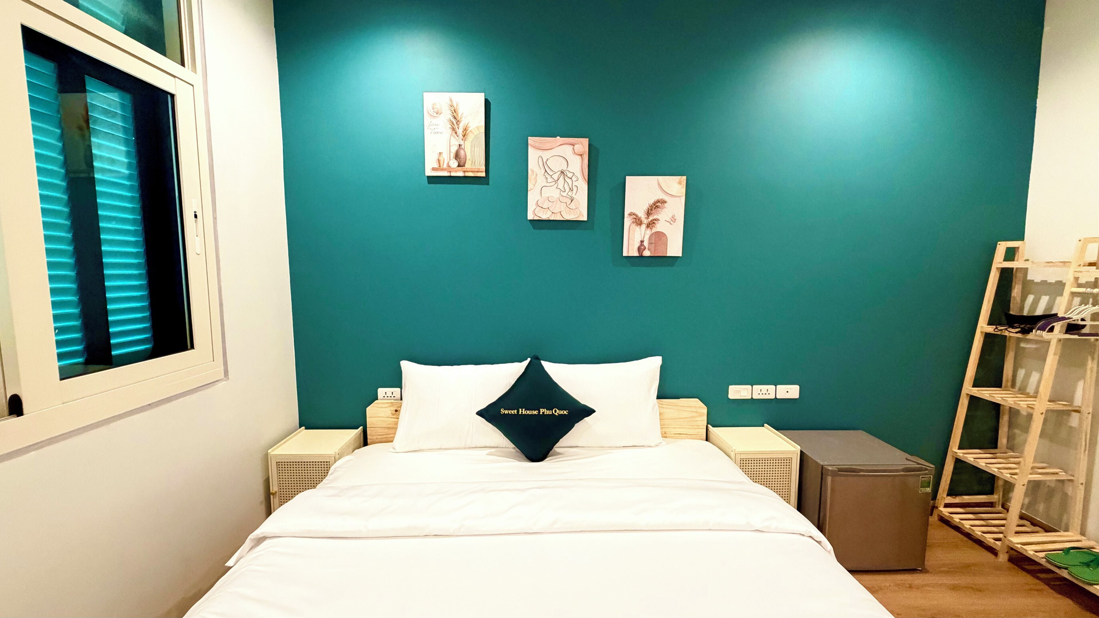 Quarto com parede em tom de verde-água, cama com roupa de cama branca e três obras de arte penduradas na parede.