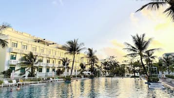 Área de piscina de hotel com várias espreguiçadeiras e palmeiras.