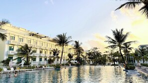 A hotel pool area with multiple lounge chairs and palm trees.