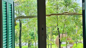 A window with a view of a green lawn, trees, and a swing set. - Sweet House Phu Quoc (Phu Quoc)