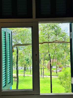Una ventana con vista a un césped verde, árboles y un columpio.