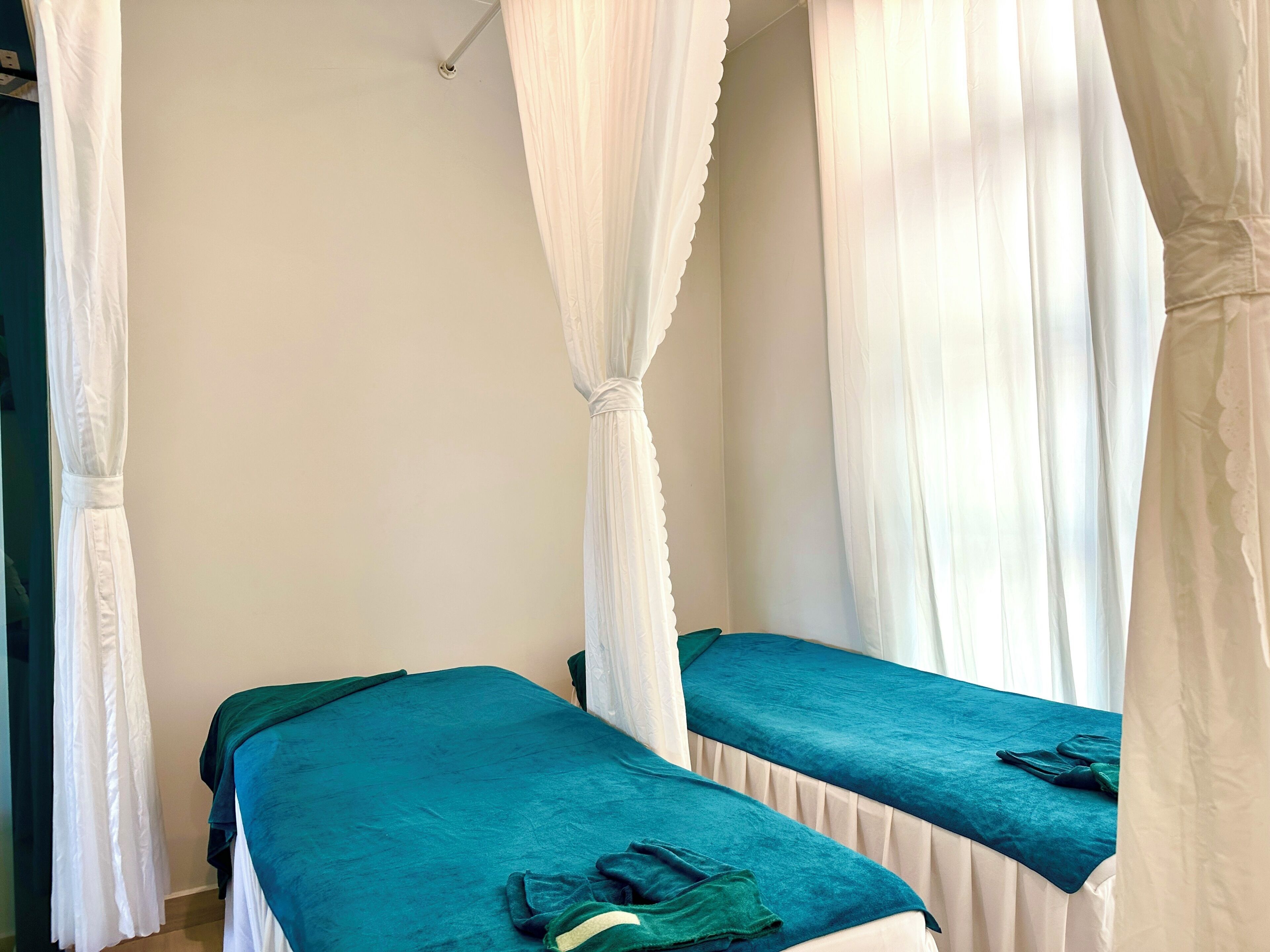 Quarto com duas camas, cada uma com colcha verde-água e cortinas brancas.