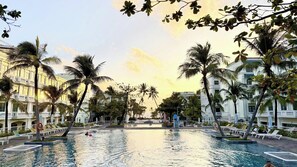 Piscina com palmeiras e um edifício ao fundo.