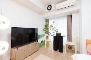A modern hotel room with a flat-screen TV, a dining table with chairs, a potted plant, and a large window with curtains. - Tora Hotel Kitashinjuku (Tokyo)