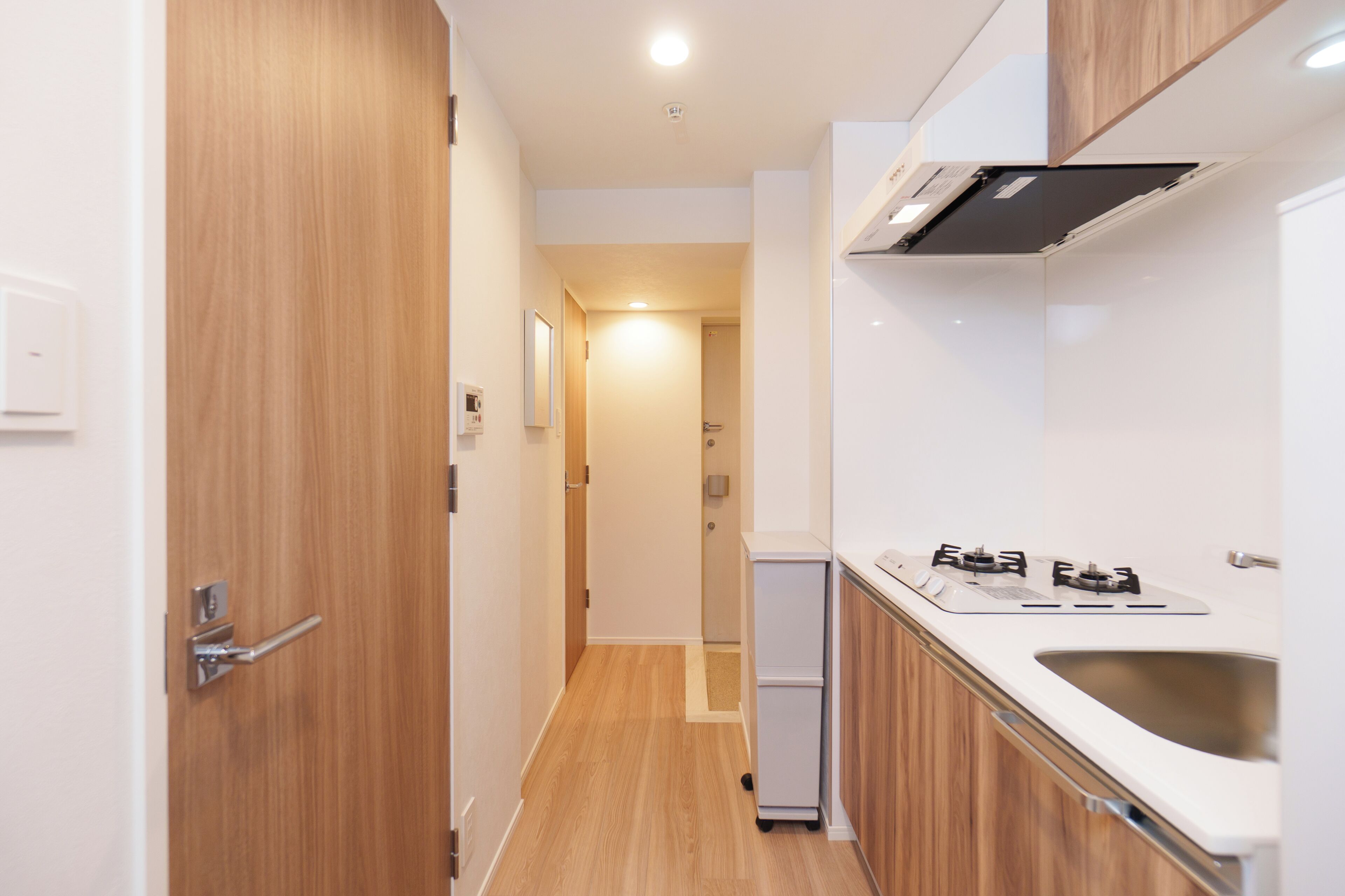A narrow kitchen with wooden cabinetry, a white countertop, and a stainless steel sink.