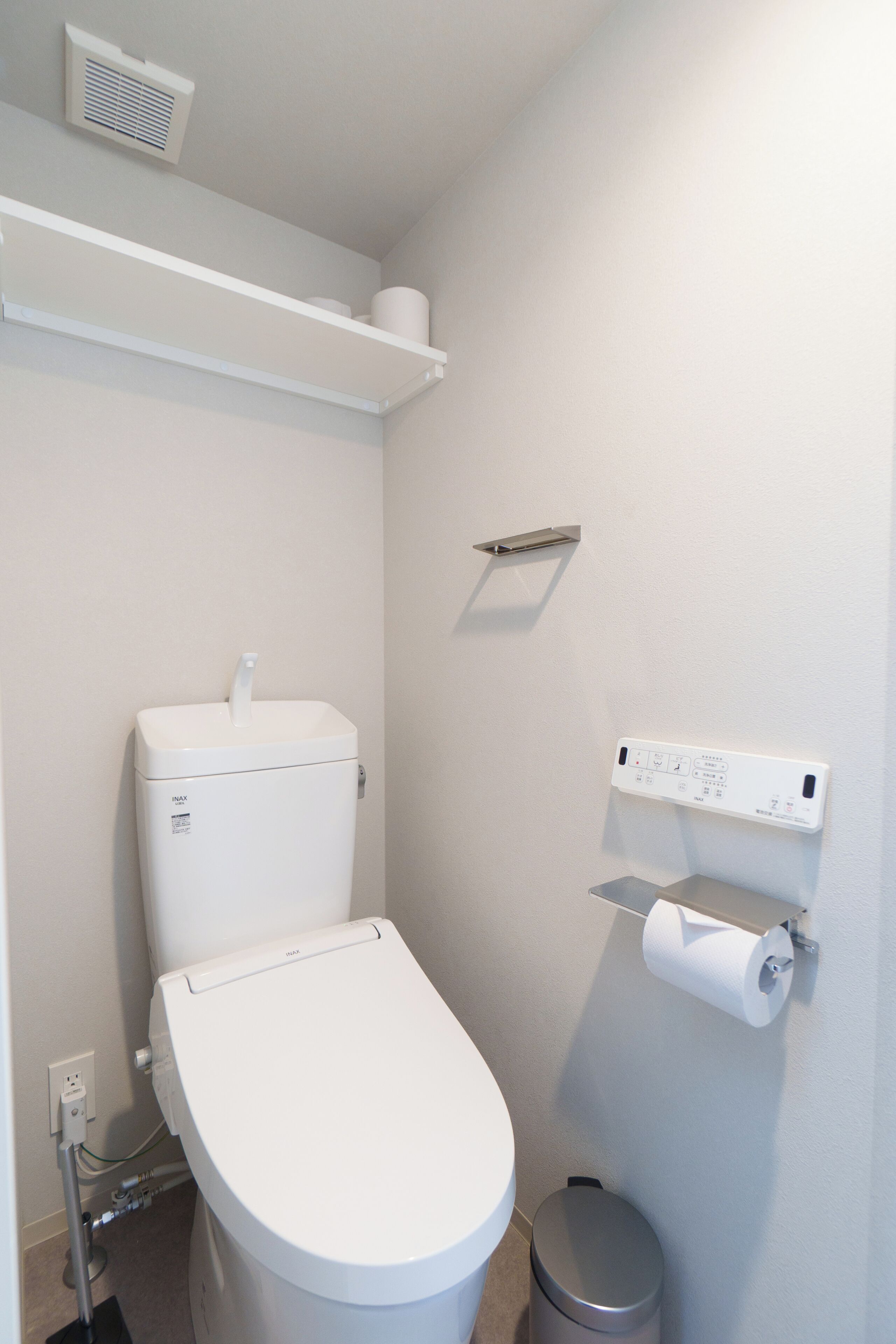 A small, modern bathroom with a toilet, a trash bin, and a toilet paper holder on the wall.