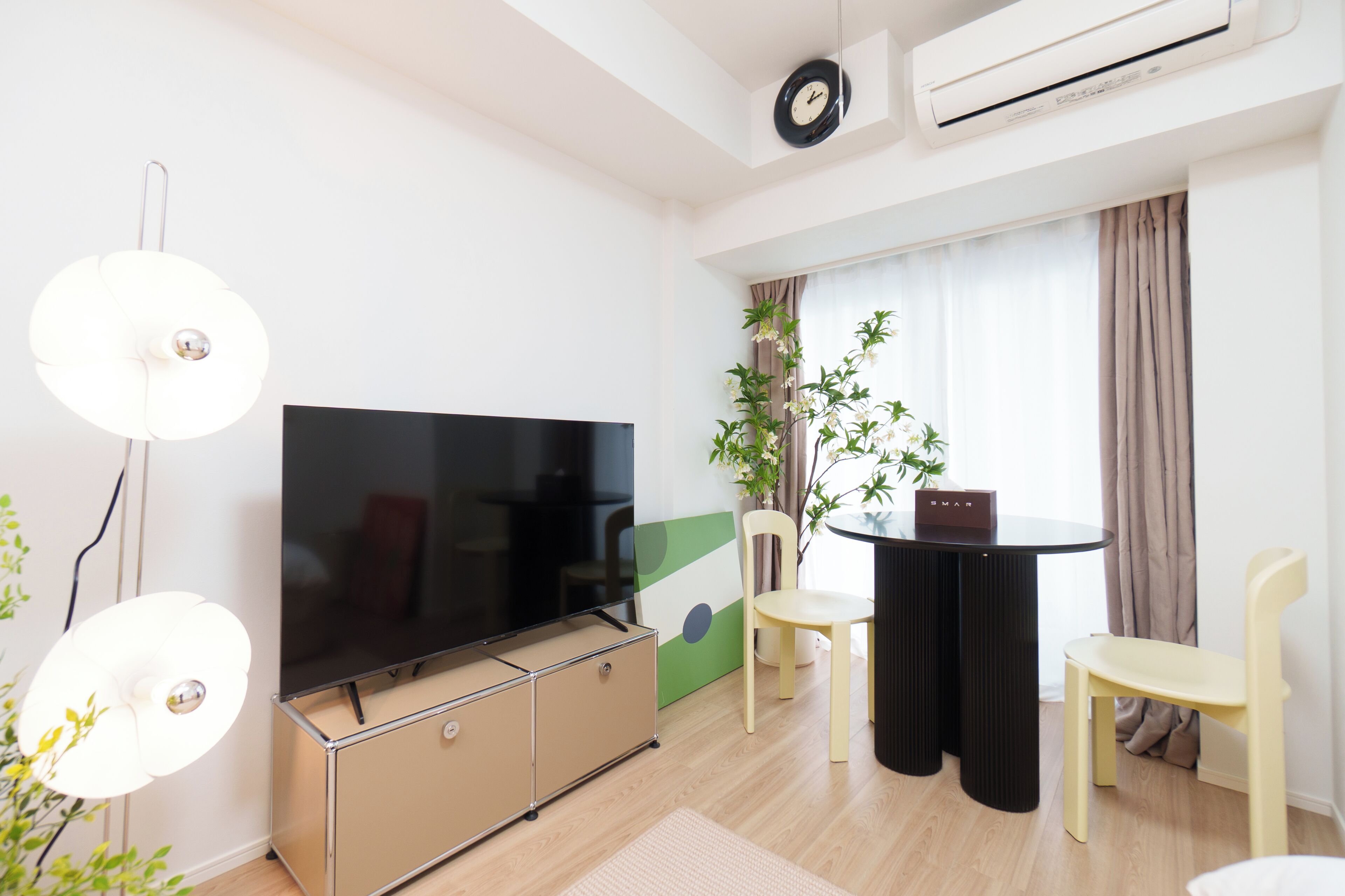 A modern living room with a flat-screen TV, a dining table with chairs, a potted plant, and an air conditioning unit.