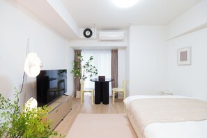Habitació d'hotel amb un llit, un televisor, una taula de treball amb dues cadires, una planta en test i una finestra amb cortines.