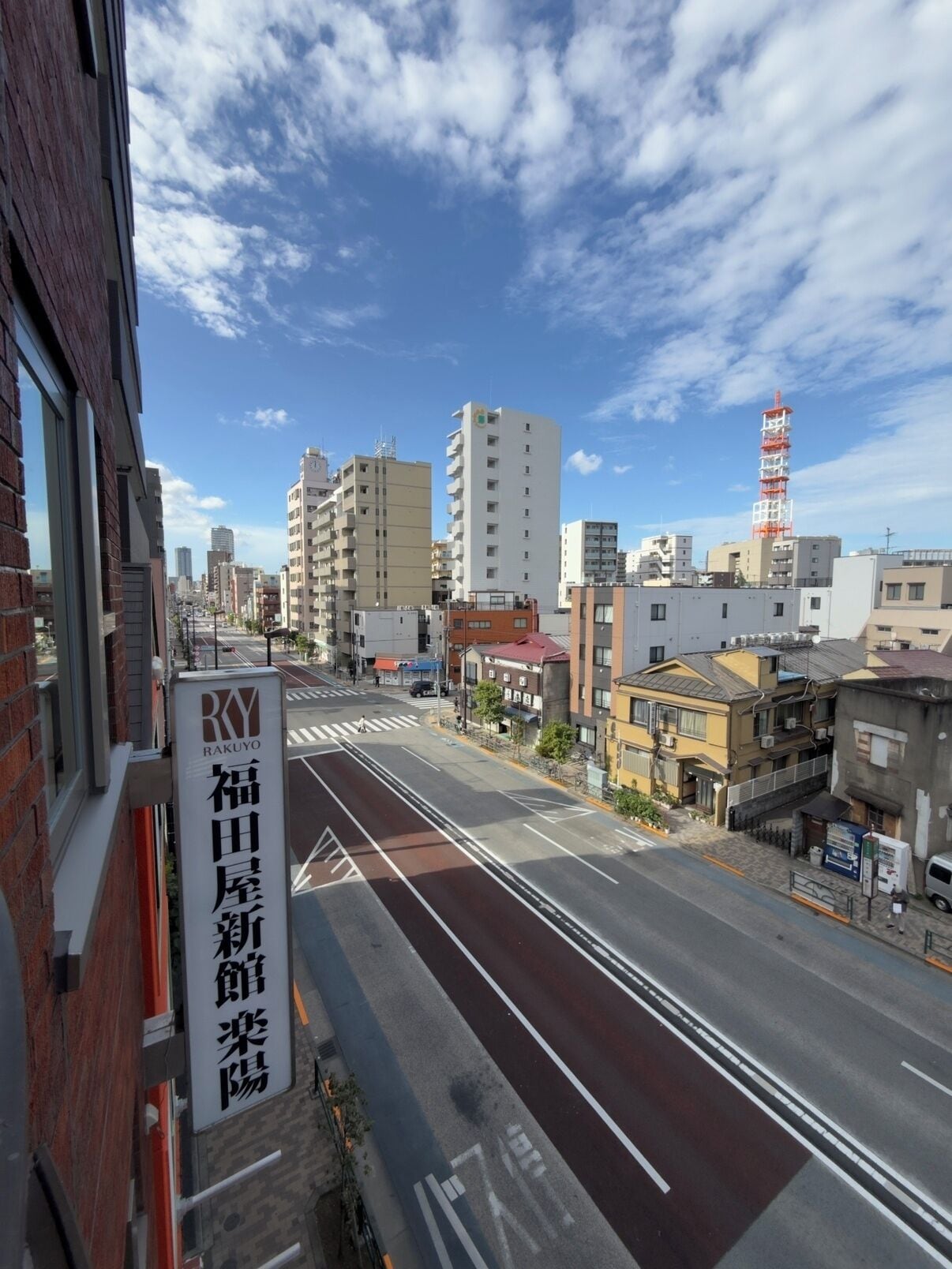 Straßenansicht mit einem Gebäude mit der Aufschrift 'RAKUYO' und blauem Himmel.