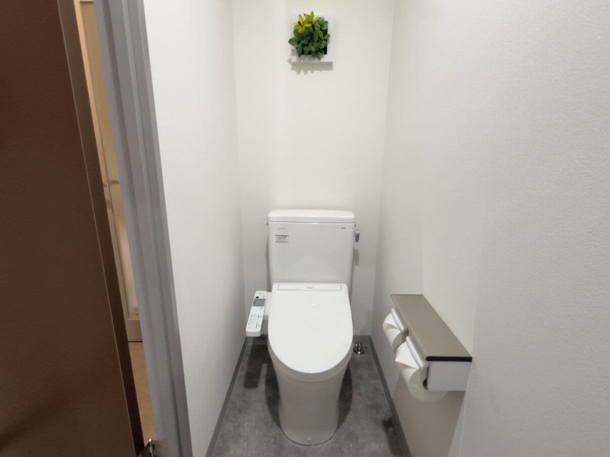 Une petite salle de bain étroite, avec des toilettes, un sèche-mains et une petite plante accrochée au mur.