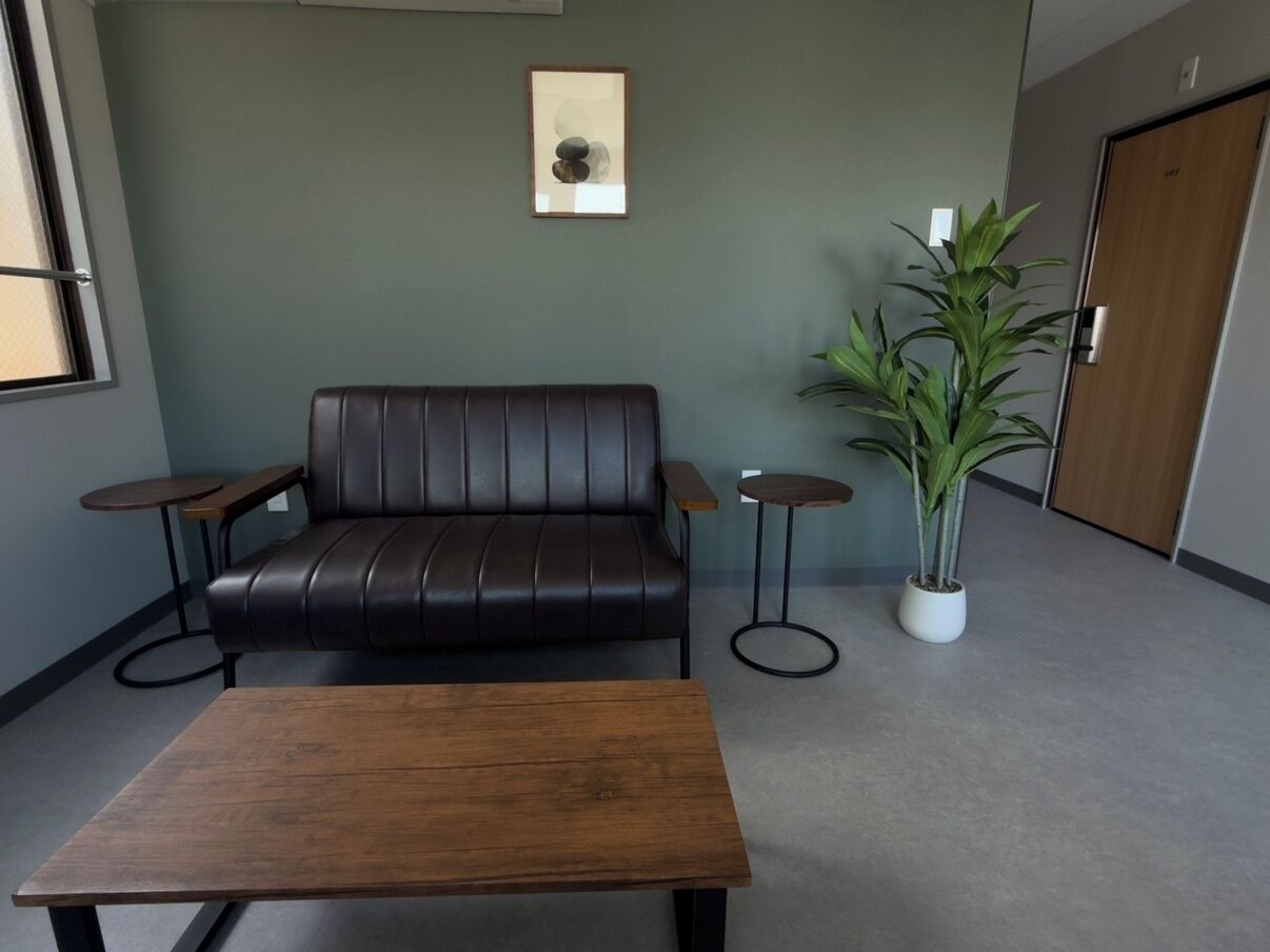 Ein Zimmer mit einer Ledersofa, einem Holztisch, zwei kleinen Beistelltischen, einer Topfpflanze und einem gerahmten Bild an der Wand.