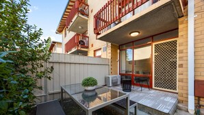 Ein Glastisch mit einer Topfpflanze, eine kleine Außenlounge mit Stühlen und ein Gebäude mit einem Balkon.