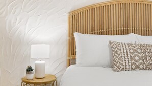 Ein Schlafzimmer mit strukturierter Wand, einem Holz-Kopfteil, einem runden Nachttisch aus Gold, einer weißen Lampe und einem gemusterten Kissen.