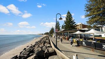A coastal promenade with a rocky shoreline, a pedestrian path, and outdoor seating areas.