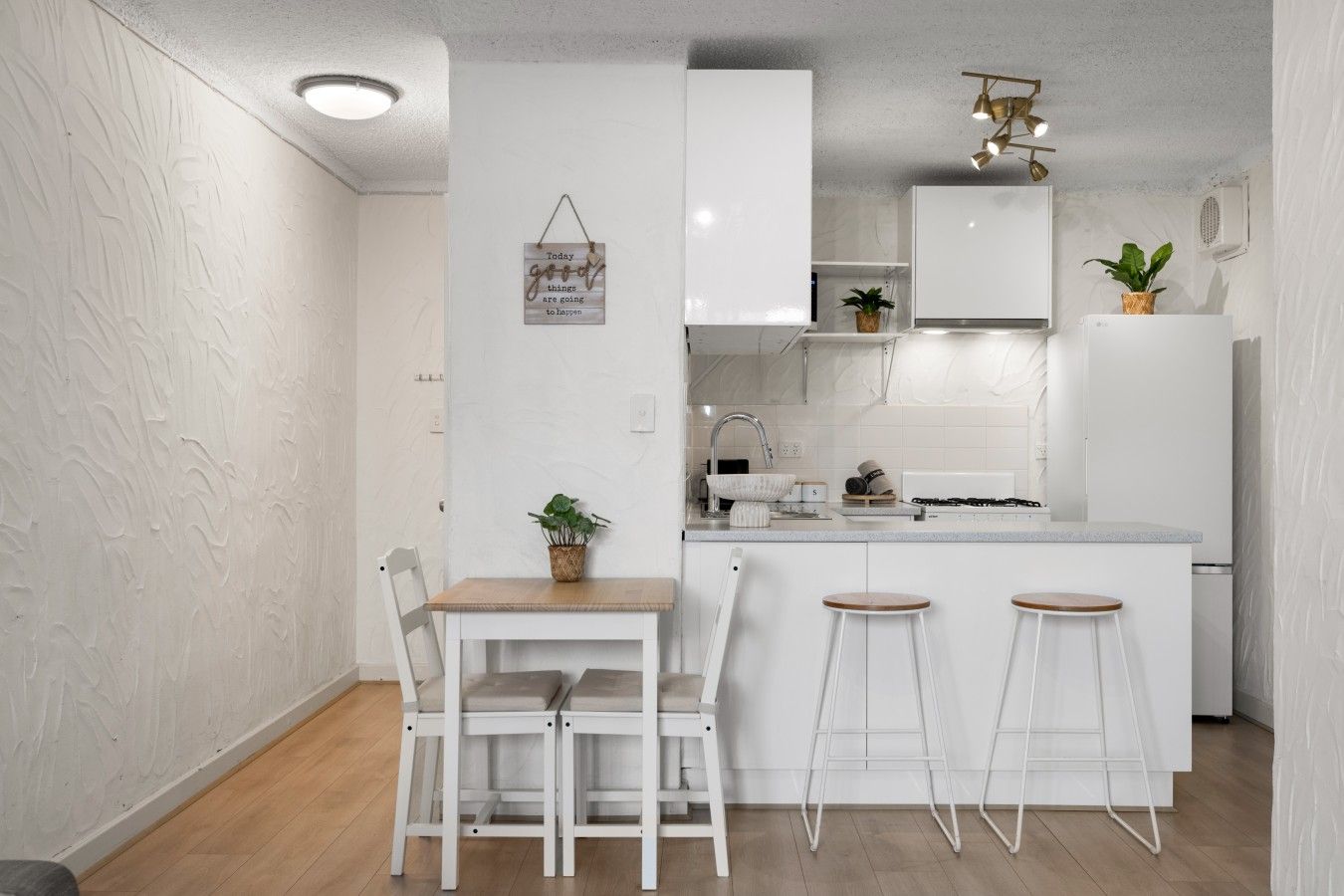 A modern kitchen with white cabinetry, a wooden dining table, and two bar stools.