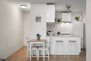Una cocina moderna con armarios blancos, una mesa de comedor de madera y dos taburetes de bar.