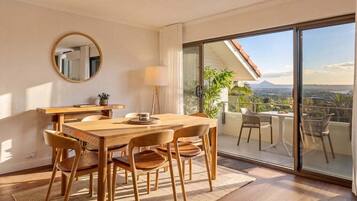 Ein Essbereich mit Holztisch und -stühlen, einem runden Spiegel an der Wand und Blick auf einen Balkon mit Gartenmöbeln.