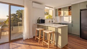 A modern kitchen with a large island, bar stools, and a sliding glass door leading to a balcony.