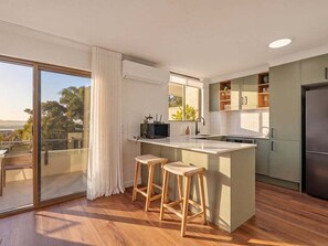 A modern kitchen with a large island, bar stools, and a sliding glass door leading to a balcony.