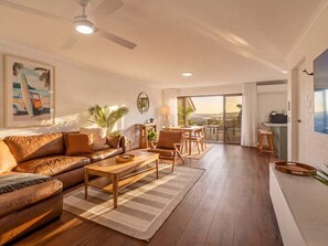 A spacious living area with a sofa, coffee table, and chairs, a dining area with a table and chairs, and a view through a glass door.