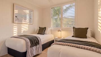 Ein Schlafzimmer mit zwei Betten, einem Deckenventilator, einem Fenster mit Jalousien und einer Nachttischlampe.