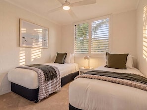 A bedroom with two beds, a ceiling fan, a window with blinds, and a bedside lamp. - Noosa International Apartment 117 - Sunset Views & Resort Luxury in the Heart of Noosa (Noosa)