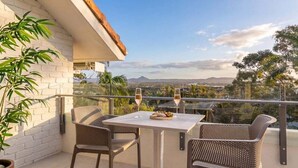 A balcony with a table and chairs, a potted plant, and a view of the landscape.