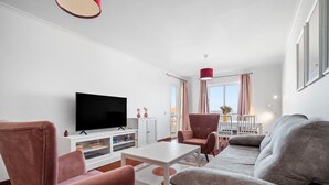 Uma sala de estar moderna com televisão de tela plana, um sofá, duas poltronas, uma mesa de centro e um espaço de refeições com mesa e cadeiras.