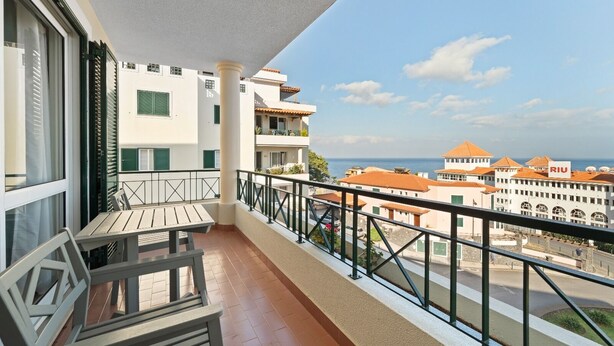 Varanda com mesa e cadeiras, com vista para uma cidade costeira, com edifícios e céu claro.