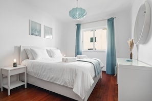 Ein Schlafzimmer mit Bett, Nachttisch, Fenster mit Vorhängen und einem Spiegel.