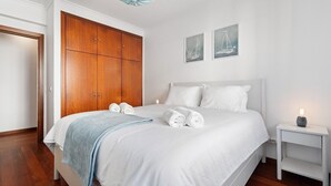 Quarto com uma cama grande, um guarda-roupa, duas obras de arte na parede e uma mesa de cabeceira com abajur.