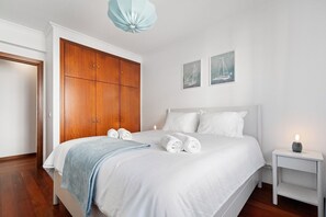 Ein Schlafzimmer mit einem großen Bett, einem Kleiderschrank, zwei Wandbildern und einem Nachttisch mit einer Lampe.