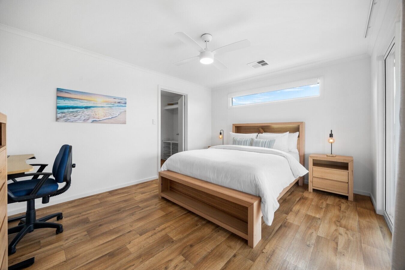 A bedroom with a bed, a desk, a chair, a nightstand, a ceiling fan, and a window.