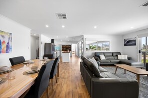 A modern interior with a dining area, a sofa, and a kitchen in the background. - A Swell Time—Spacious Garden Haven by the Coast (Goolwa Beach)