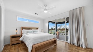 A bedroom with a bed, wooden nightstands, a ceiling fan, and a view through a sliding glass door. - A Swell Time—Spacious Garden Haven by the Coast (Goolwa Beach)