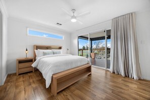 A bedroom with a bed, wooden nightstands, a ceiling fan, and a view through a sliding glass door. - A Swell Time—Spacious Garden Haven by the Coast (Goolwa Beach)