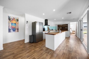 Eine moderne Küche mit einer zentralen Kochinsel, einem Kühlschrank und einem Essbereich mit einer Holzausziehtafel.