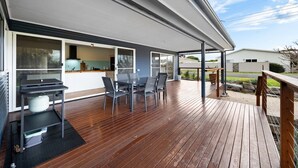 A covered outdoor area with a wooden deck, a table with chairs, and a grill. - A Swell Time—Spacious Garden Haven by the Coast (Goolwa Beach)