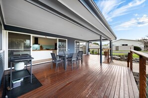 A covered outdoor area with a wooden deck, a table with chairs, and a grill. - A Swell Time—Spacious Garden Haven by the Coast (Goolwa Beach)