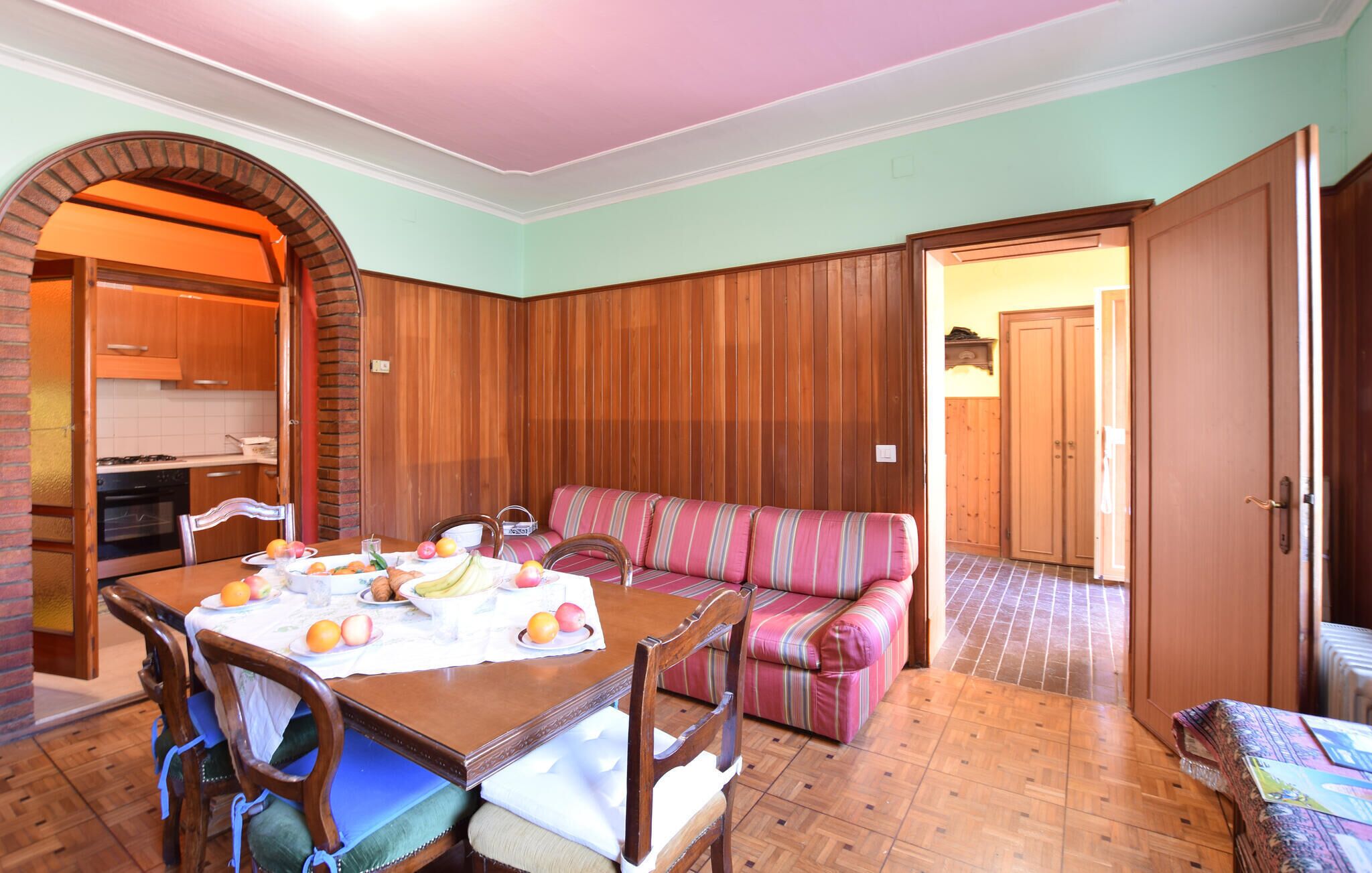 A dining area with a wooden table set for breakfast, a striped sofa, and a kitchen visible through an archway.