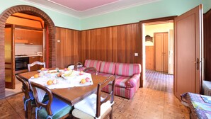 Ein Essbereich mit Holztisch, gedecktem Frühstücksservice, einem gestreiften Sofa und einer durch einen Bogen sichtbaren Küche.
