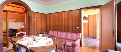 A dining area with a wooden table set for breakfast, a striped sofa, and a kitchen visible through an archway.