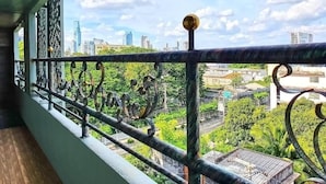 A balcony with a metal railing overlooking a cityscape with buildings and greenery.