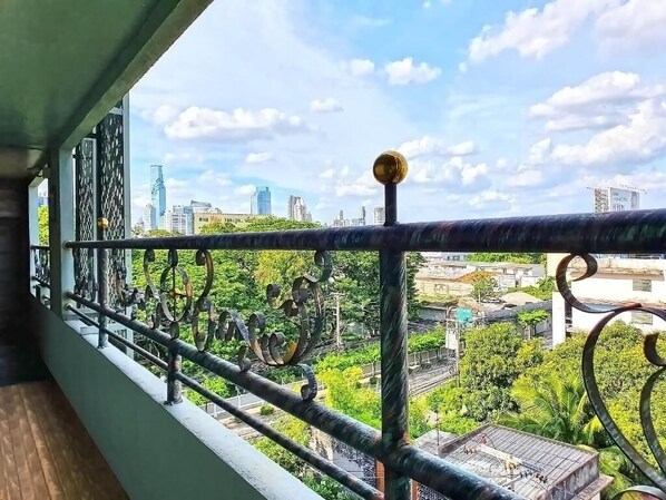 A balcony with a metal railing overlooking a cityscape with buildings and greenery.