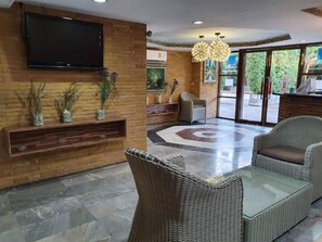 Un vestíbulo con televisión de pantalla plana, muebles de mimbre, piso estampado y mostrador de recepción.