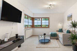 A modern living room with a flat-screen TV, a glass coffee table, a sofa, and a potted plant.